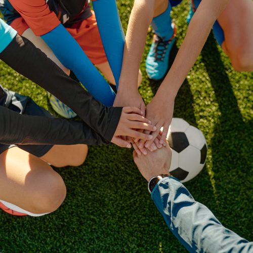 Football coach motivating junior football team before match stacking hands on ball together