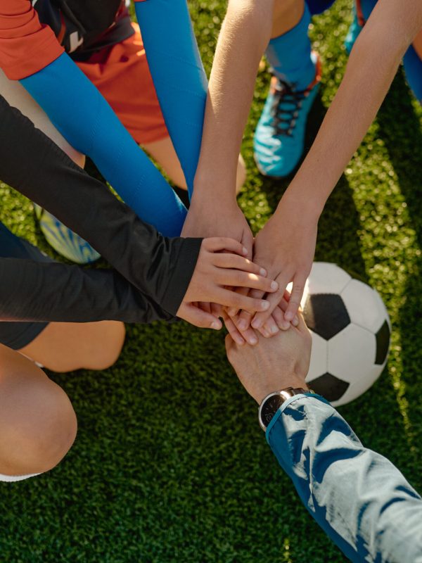 Football coach motivating junior football team before match stacking hands on ball together