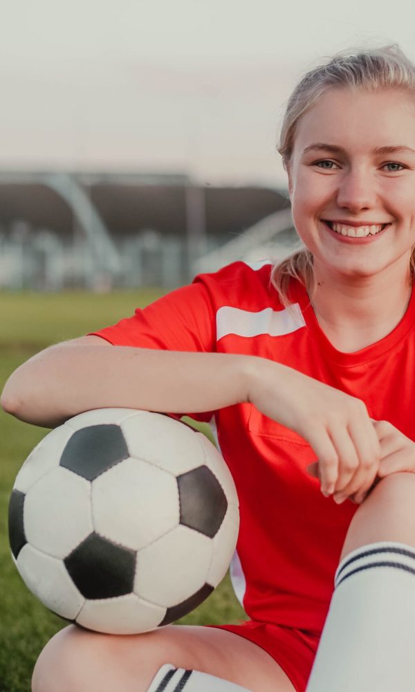 Portrait of smiling girl soccer player with ball sitting on the grass